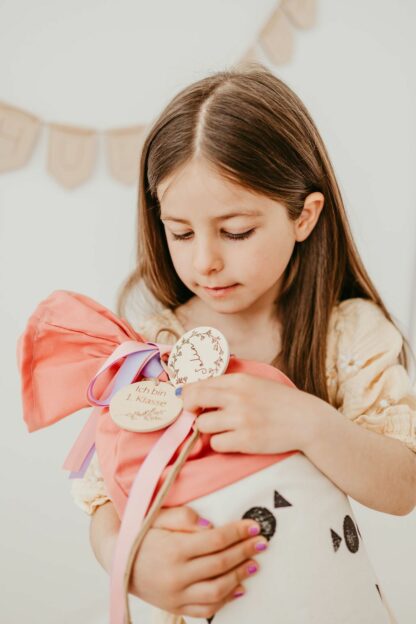 Auf diesem Bild sieht man ein Mädchen mit einer Schultüte und Anhängern mit Namen.