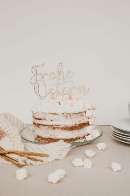 Auf diesem Bild ist eine Torte mit einem Cake Topper aus Holz mit dem Schriftzug Frohe Ostern zu sehen.