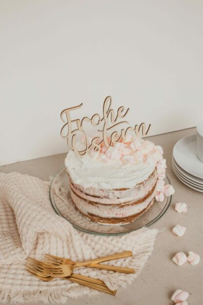 Auf dem Bild sieht man einen Kuchen, der mit einem Holz Cake Topper mit dem Schriftzug Frohe Ostern dekoriert ist.