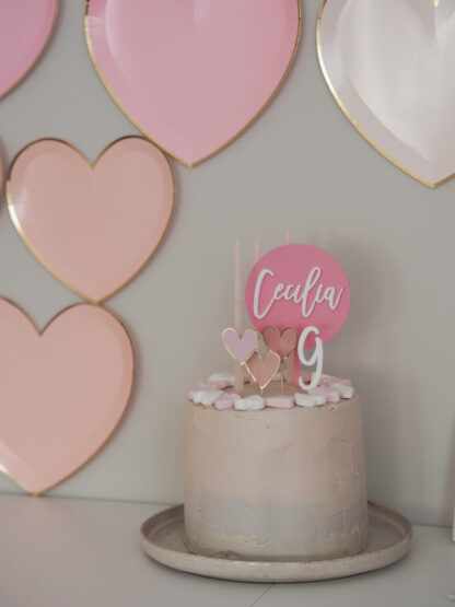 Auf dem Bild sieht man eine Torte mit Herzen dekoriert und einem personalisierten Cake Topper in rosa aus Acryl.