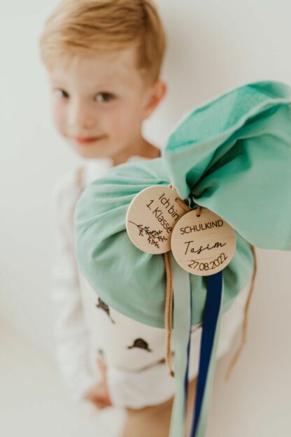 Auf diesem Bild sieht man einen Jungen der eingeschult wird und eine Schultüte von tinyday mit Anhängern mit Namen in der Hand hält.