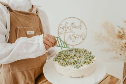 Auf diesem Bild sieht man eine Kinderhand die einen Cake Topper zur Einschulung in eine Torte steckt.