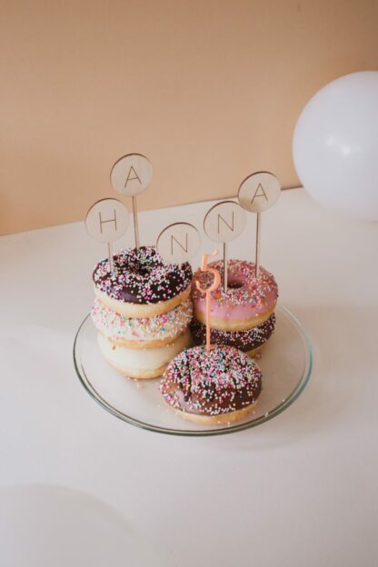 Auf dem Bild sieht man Donuts mit Streuseln und einem Cake Topper aus Acryl mit einer Zahl.