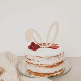 Auf diesem Bild ist eine Torte mit einem Cake Topper aus Holz in Form von Hasenohren zu sehen.