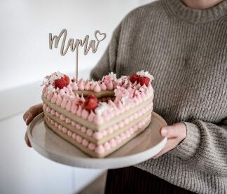 Auf diesem Bild siehst du einen Kuchen in Form eines Herzes mit einem Cake Topper Mama dekoriert.