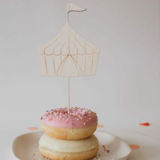 Auf diesem Bild sieht man einen Donut mit einem Cake Topper Zirkuszelt aus Holz.