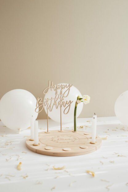 Auf diesem Bild sieht man einen Geburtstagskranz mit Blumen, Kerzen und einen Namen aus Holz.