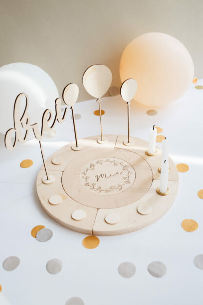 Auf diesem Bild sieht man Luftballons aus Holz in einem Geburtstagskranz dekoriert.