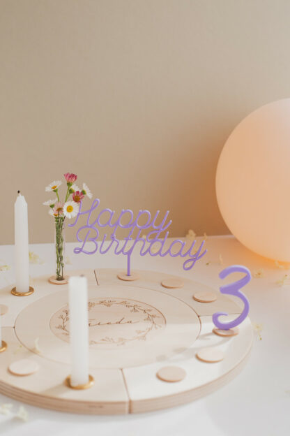 Auf diesem Bild sieht man einen Geburtstagskranz in bunt mit lila Zahlen und Happy Birthday Stecker.