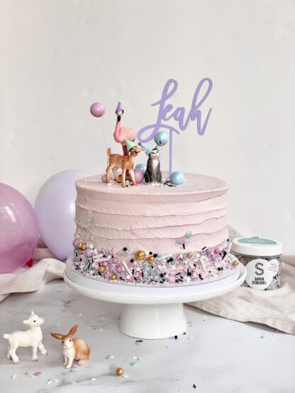 Auf diesem Bild sieht man einen bunten Cake Topper mit Namen in einem Kuchen mit Schleich Tieren dekoriert.