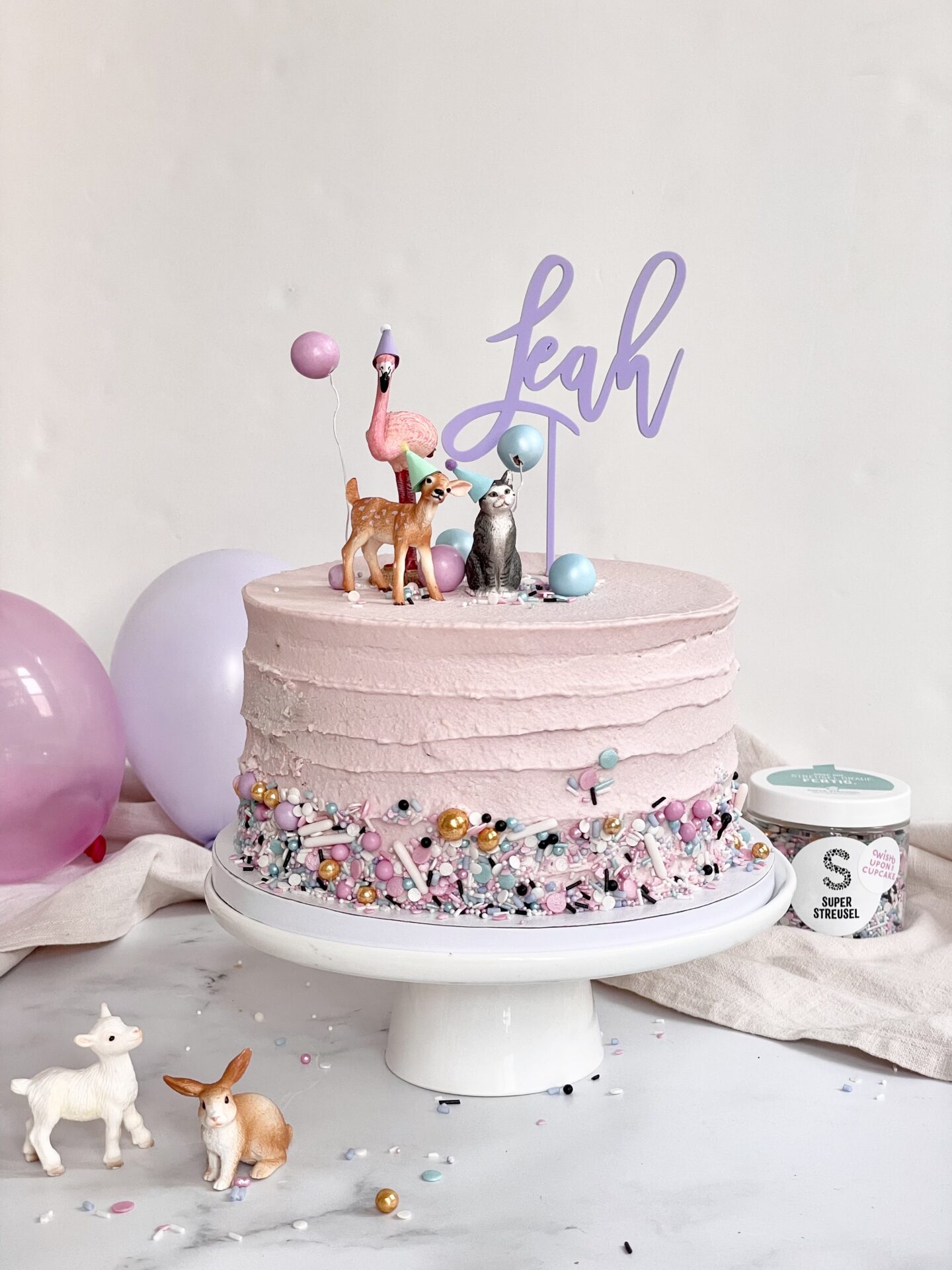 Auf diesem Bild sieht man einen bunten Cake Topper mit Namen in einem Kuchen mit Schleich Tieren dekoriert.