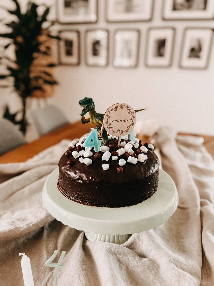 Auf diesem Bild sieht man eine Schoko Torte mit einem Dino und einem personalisierten Holz Cake Topper.