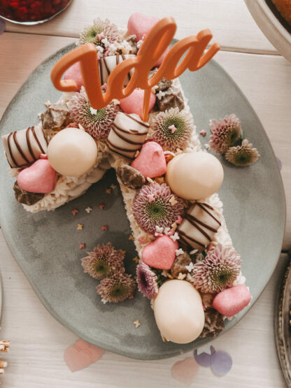 Auf dem Bild sieht man einen bunten Cake Topper mit Namen zum ersten Geburtstag in einem Kuchen.