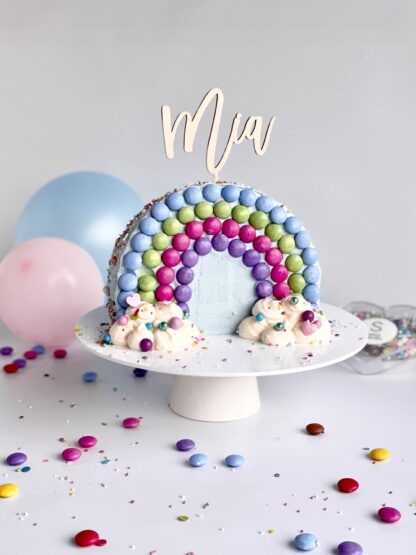 Auf diesem Bild sieht man einen personalisierten Cake Topper in einem Regenbogen Kuchen.